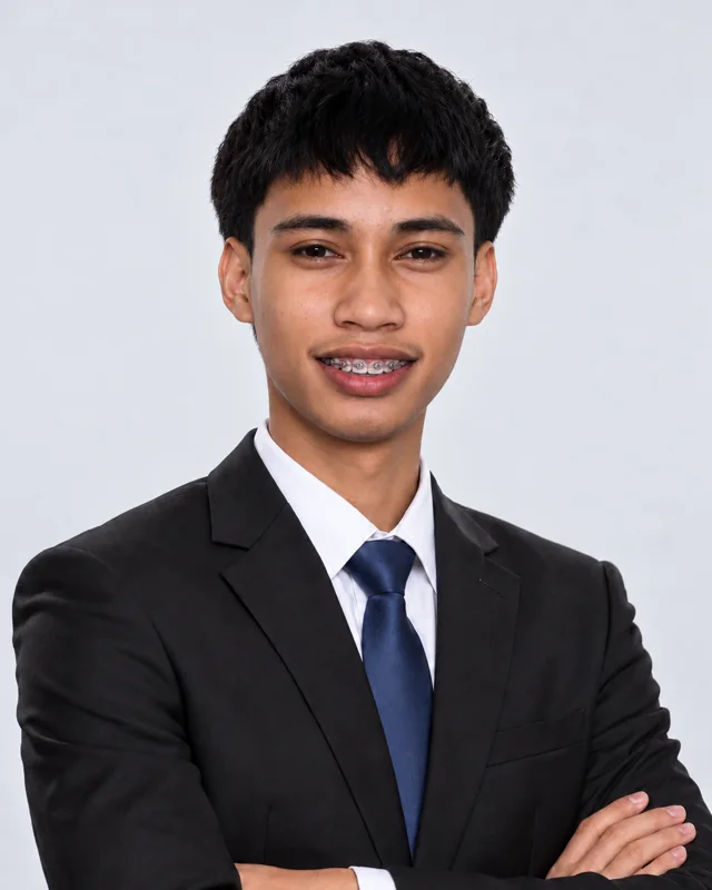 Rhod in a dark suit and navy tie, arms crossed, smiling